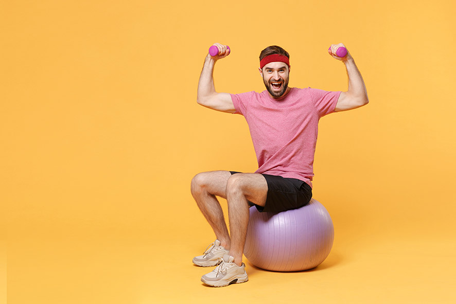 un homme assis sur un ballon fait des exercices avec des altères